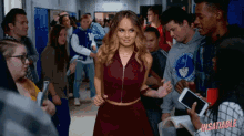 a woman in a red dress is standing in a hallway surrounded by people with the word insatiable on the bottom right