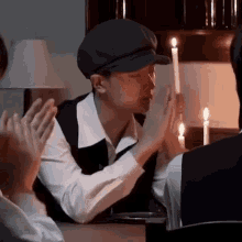 a man wearing a hat and a vest is sitting at a table with candles .