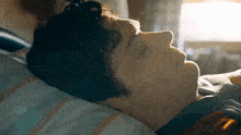 a young man is laying in bed with his eyes closed and the sun is shining through the window .