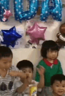 a group of children are sitting in front of a wall with balloons and a sign that says ' a ' on it