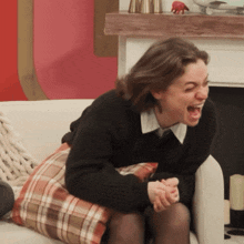 a woman in a black sweater sits on a couch laughing