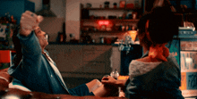 a man and a woman are sitting at a table in front of a red sign that says on