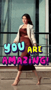a woman in a brown dress is standing in front of a sign that says ' you are amazing '