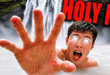 a man is swimming in a waterfall and reaching out his hand towards the camera .