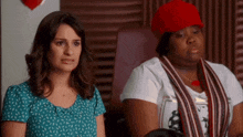 two women are sitting next to each other and one has a red hat on