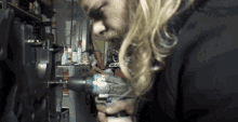 a man with long blonde hair is using a drill to fix something
