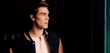 a young man wearing a purple varsity jacket and a white shirt is standing in front of a green curtain .