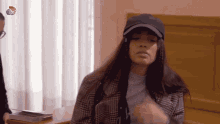 a woman wearing a hat and a plaid jacket is sitting in front of a window