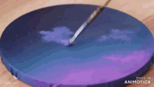 a person is painting a purple and blue sky with a brush on a round canvas