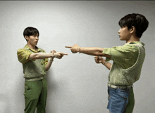 two young men pointing at each other in front of a wall