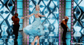 a woman in a blue dress is dancing on stage with two men