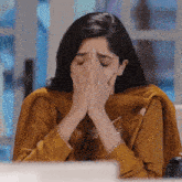 a woman in a yellow dress is covering her face with her hands while sitting in front of a laptop computer .