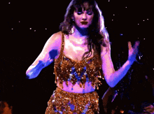 a woman in a gold crop top and skirt is holding a microphone