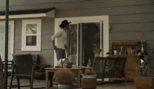 a man in a cowboy hat is standing on a porch in front of a house