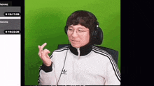 a man wearing headphones and a white adidas jacket giving a thumbs up