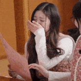a girl is covering her mouth with her hand while holding a piece of paper