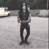 a man in a black and white costume is standing in a parking lot with a white van in the background .