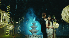 a man and woman standing in front of a fountain at night