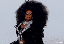 a drag queen with a very large afro is wearing a black and silver dress