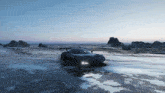 a black sports car is driving on a snowy beach near the ocean