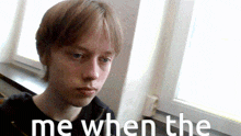a young man sitting in front of a window with the words " me when the " written on the bottom