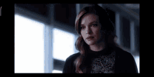 a woman with long red hair is standing in front of a window and looking at the camera .
