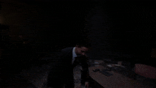 a man in a suit is standing in a dark room talking to another man