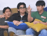 three young men are sitting on a couch with pillows and one of them is making a funny face .
