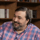 a man with a beard wearing a plaid shirt and earrings smiles