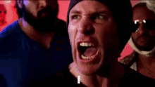 a man wearing a beanie is talking to a group of people and the word love is on his face .