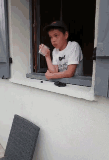 a young boy looks out of a window while holding a glass