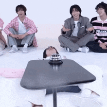 a man wearing a frank hoodie sits on the floor with other people