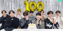 a group of young men are posing for a picture in front of a cake and balloons that say 100