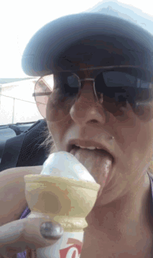 a woman wearing sunglasses and a hat is licking an ice cream cone with a q on it
