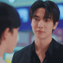 a man in a black suit looks at another man in a black shirt