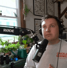 a man wearing headphones and a chuck sandwich shirt is talking into a rode microphone