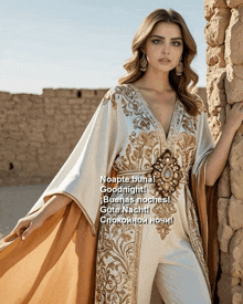 a woman in a white and gold dress is standing next to a stone wall