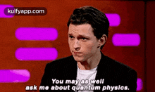 a man in a suit and white shirt is talking to another man on a stage and asking him about quantum physics .