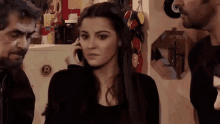 a woman is talking on a cell phone while standing next to two men
