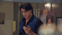a man in a blue vest is standing in a room looking at his phone .