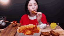 a woman in a red shirt is eating a piece of fried chicken with chopsticks