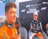 a man is talking into a microphone in front of a miami grand prix sign
