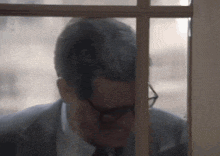 a man in a suit and tie looking out a window