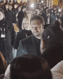 a man in a black suit stands in a crowd of people