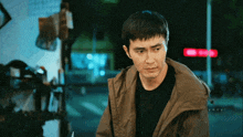 a man in a brown jacket stands in front of a red light that says ' yanzi ' on it