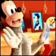 goofy is standing in front of a table with a picture of mickey mouse in the background .