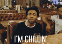 a man sitting at a table with the words " i 'm chillin " written on the bottom