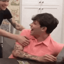 a man in a pink shirt is being hugged by another man in a kitchen .