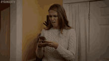 a woman in a white sweater is looking at her phone with the hashtag youngertv on the bottom