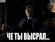 a man in a suit and tie is sitting in a dark room with the words peaky blinders in the background